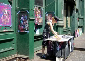 Photo by Ilse Orsel on Unsplash, Women standing in front of table selling colorful art in front of green building on street