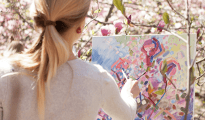 girl painting flowers outside in front of canvas