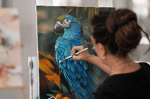 Woman painting on canvas blue and green feathers orange flowers