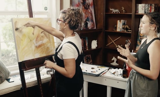 two women standing in front of an art canvas paitning in brown and yellow