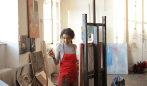 Woman standing in front of art east in red apron 