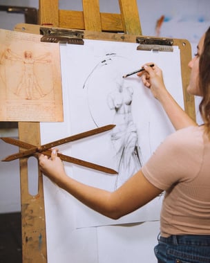 girl standing in front of paper draing a figure with drawing tool