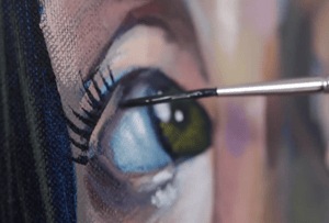 hand holding paint brush to painting of green eye