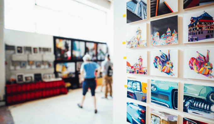 person in an art gallery with colorful small canvases on walls