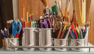 Metal containers holding various art supplies: scissors, colored pencils, brushes
