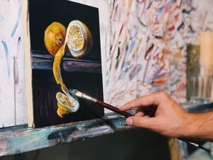 Oil painting demonstration of hand painting a yellow lemon on a black canvas