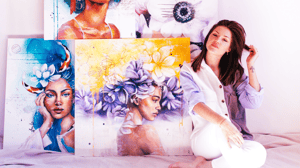 Girls in white shirt sitting in front of bold colored painted canvas portraits 