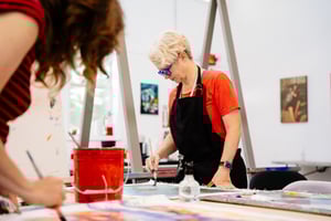 Woman in classroom in black art apron red bucket