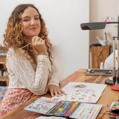 woman sitting at desk painting with watercolors 
