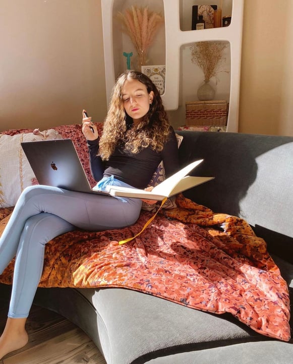 woman sitting on grey couch at computer and journal