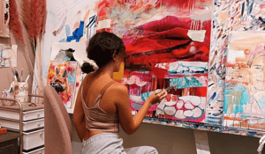 woman sitting in front of red white painting painting with paintbrush