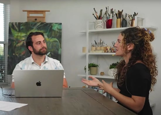 man and woman sitting at desk with computer talking working