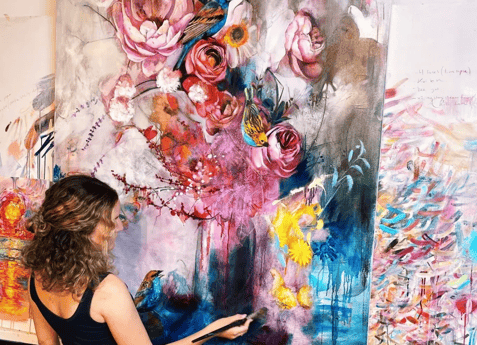 girl painting in front of bold color flower canvas pink yellow blue