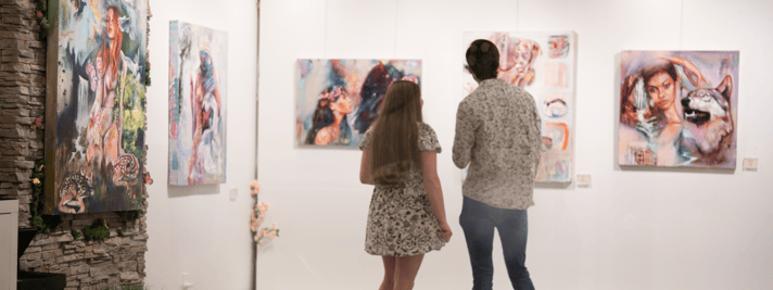 two people standing in gallery looking at paintings