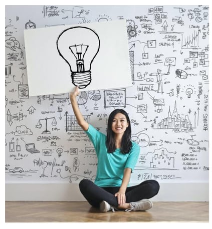woman holding poster of lightbulb sketch above her body, sketches on wall