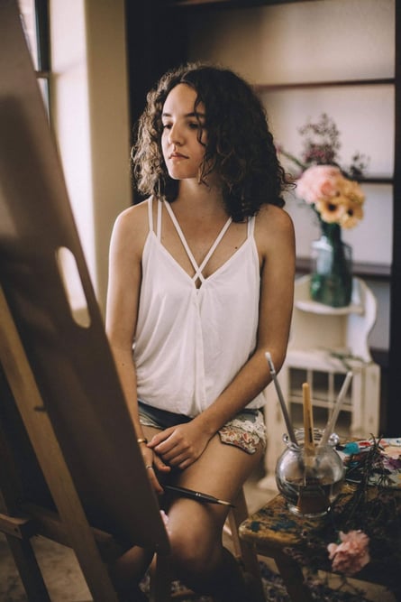 girl in white tank top sitting in front of canvas