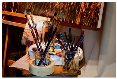 brushes in jars with paint pallet Photo caption: Setting up an art studio in a small space means making room someplace, often in the corner of a room, like the den. Image by PublicDomainPictures from Pixabay.