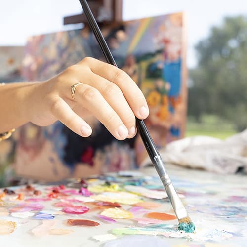 paintbrush in hand on pallet pink orange yellow paint