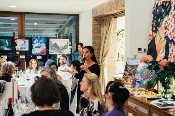 woman holding microphone taling to people in a room with art work on walls