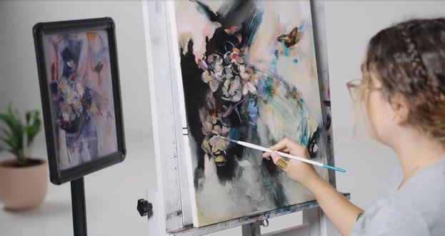 woman painting abstract flower on canvas with painting source on stand