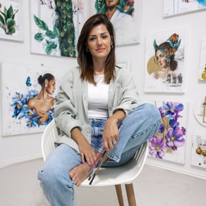 Woman sitting in gallery with colorful portraits painted behind her 