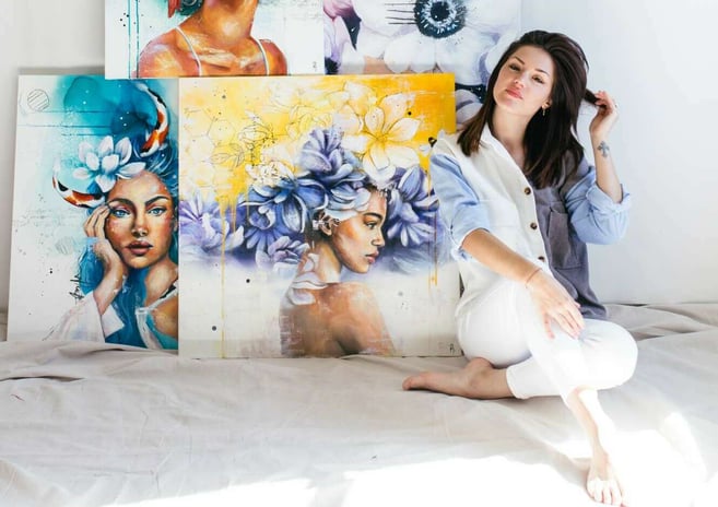 woman in blue and white sitting in gallery with colorful portraits