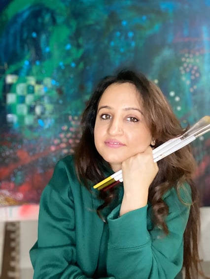 Ritika Aurora woman sititng in green top in front of colorful painitng hold milan fearless paint brushes
