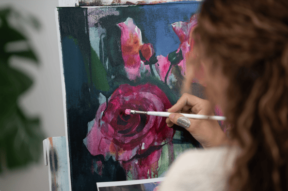 girl painting pink flowers on canvas with while handle paintbrush