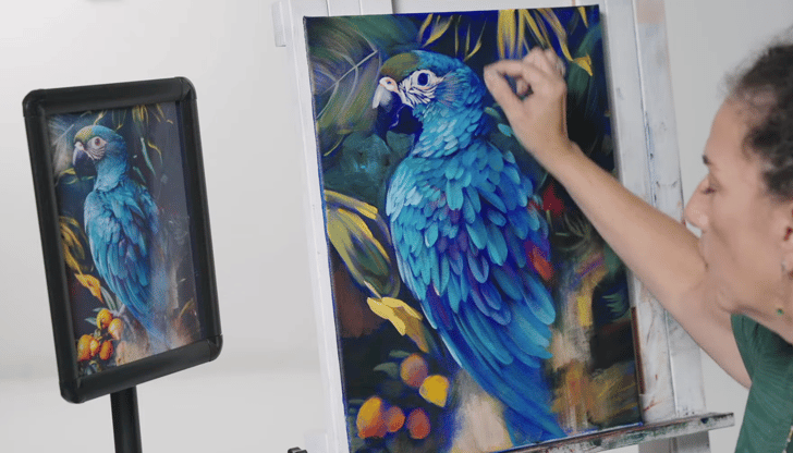 woman painting canvas blue parrot with screen and source