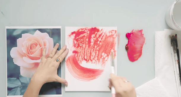 hands and paintbrush working on floral painting in pink tones