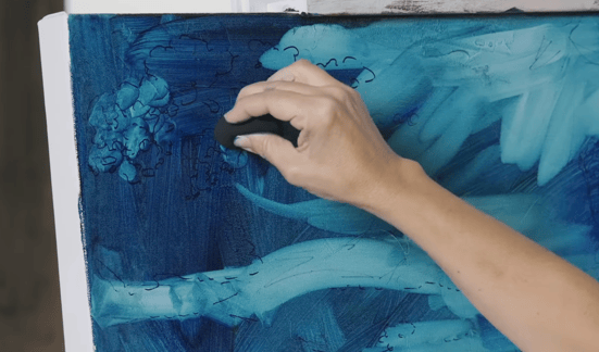 Hand subtracting blue oil paing from canvas