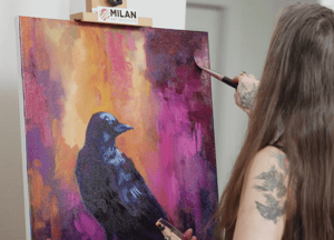 woman painting black crow with pink and orange background 