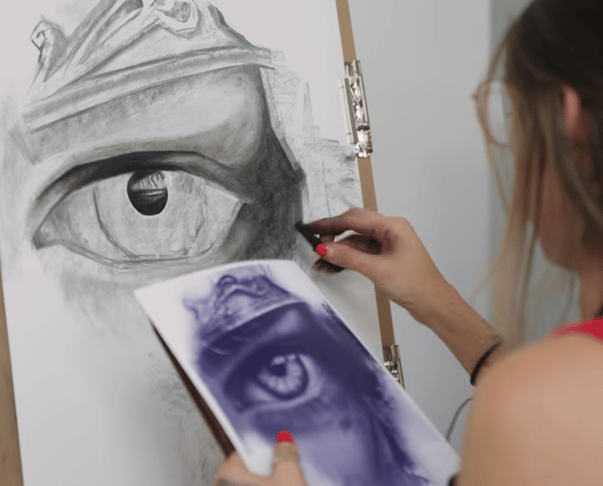 woman drawing an eye on easel board with paper source in hand