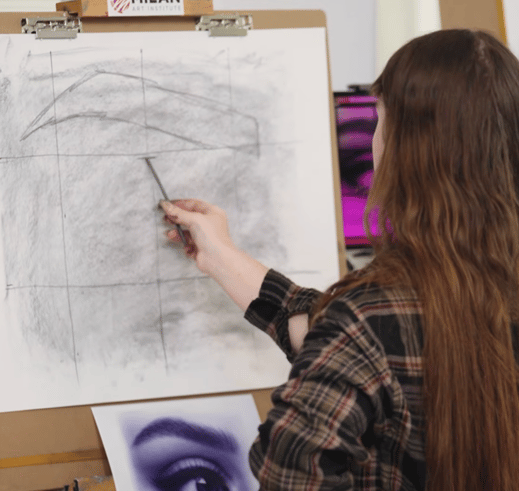woman in plaid and brown hair drawing an eye on a wood easel board