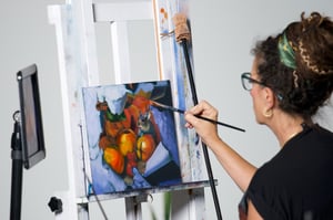 Woman painting a canvas of oranges on blue canvas