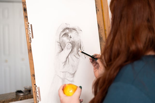 woman drawing hand holding yellow apple on easel board