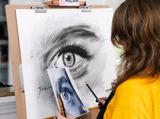 woman in yellow shirt drawing an eye on a wooden board easel