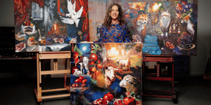 Woman sanding with painting in room surounded but other paintings