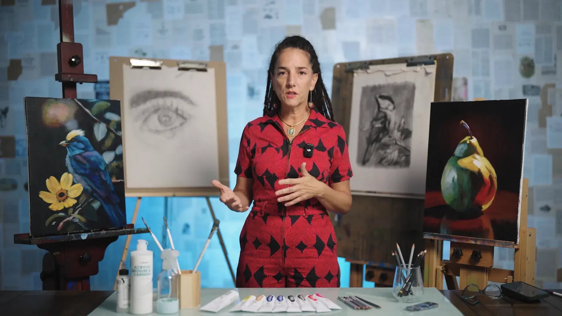 Elli Milan in her studio with the four finished pieces from the Beginner Art Program: an acrylic bird with a yellow flower, a graphite eye, a charcoal bird and an acrylic pear