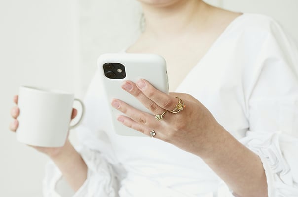 hand holding while mug and white phone in white shirt gold rings on hand