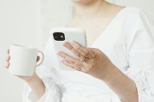 Person holding their white phone and white coffee mug