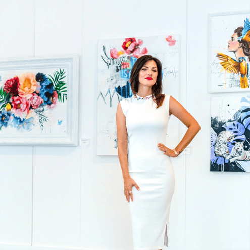 Woman in white dress standing on gallery with colorful art on walls