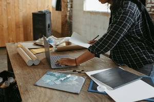 Male Artist in plaid shirt writing on computer with wooden table
