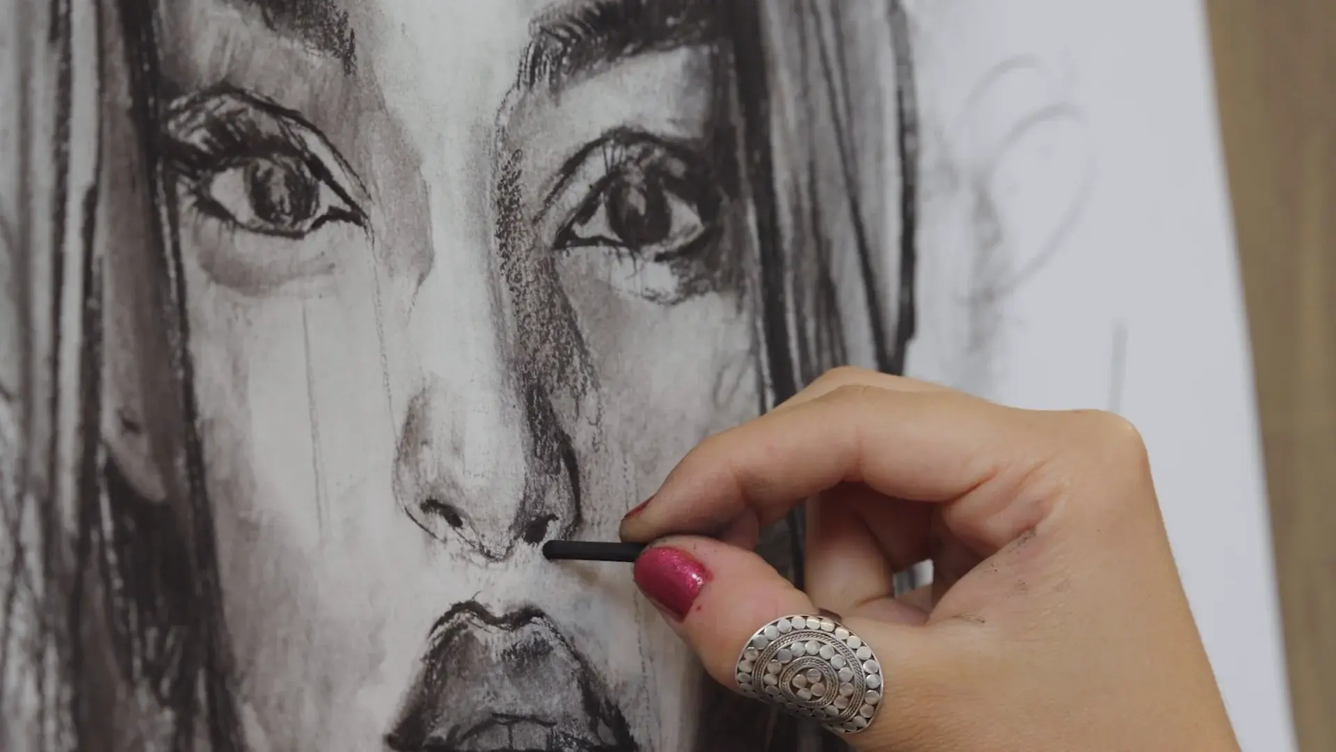Close up of a hand drawing the nostril in charcoal, the eyes above