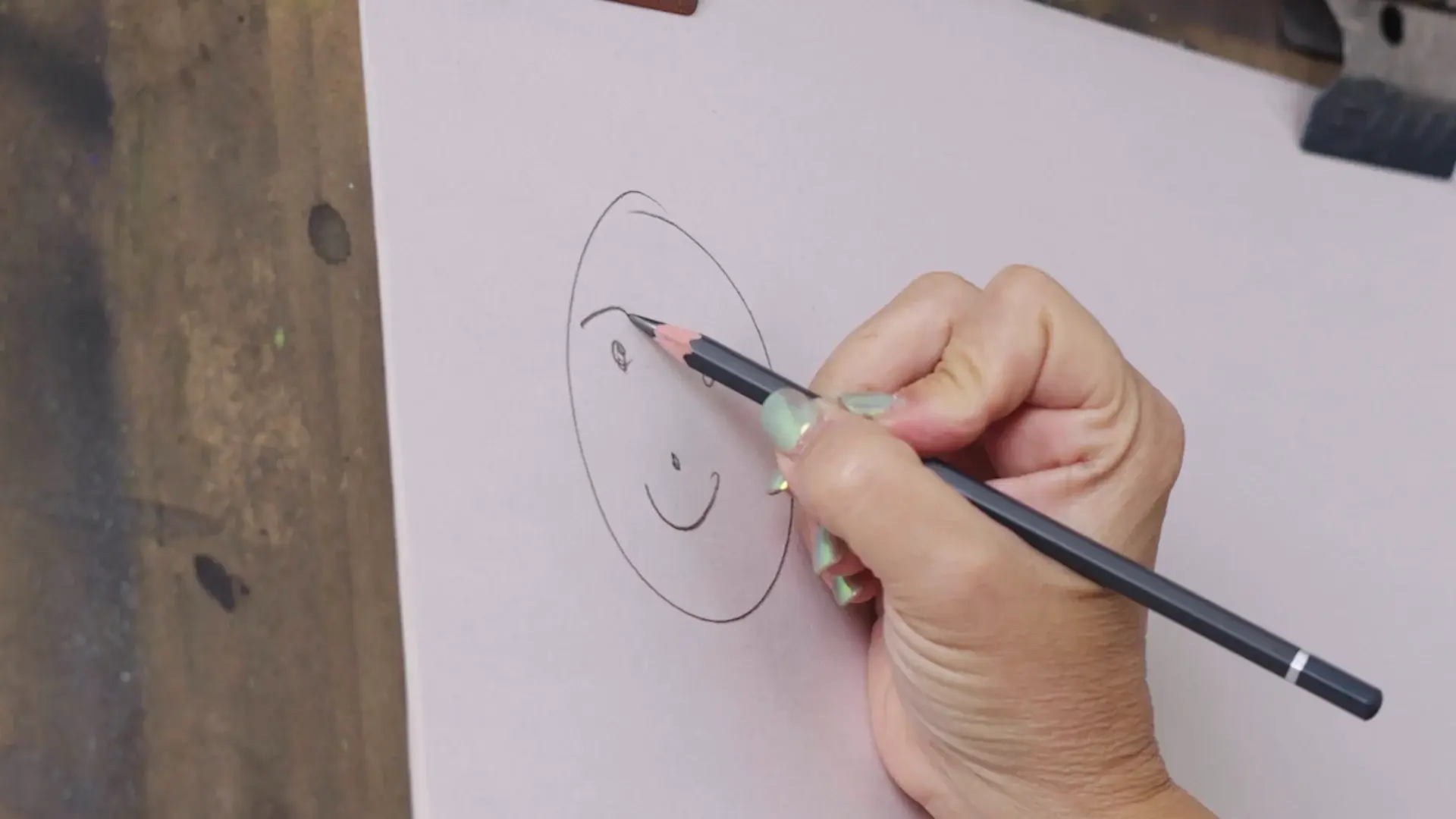 A simple oval face with a smile being drawn on white paper