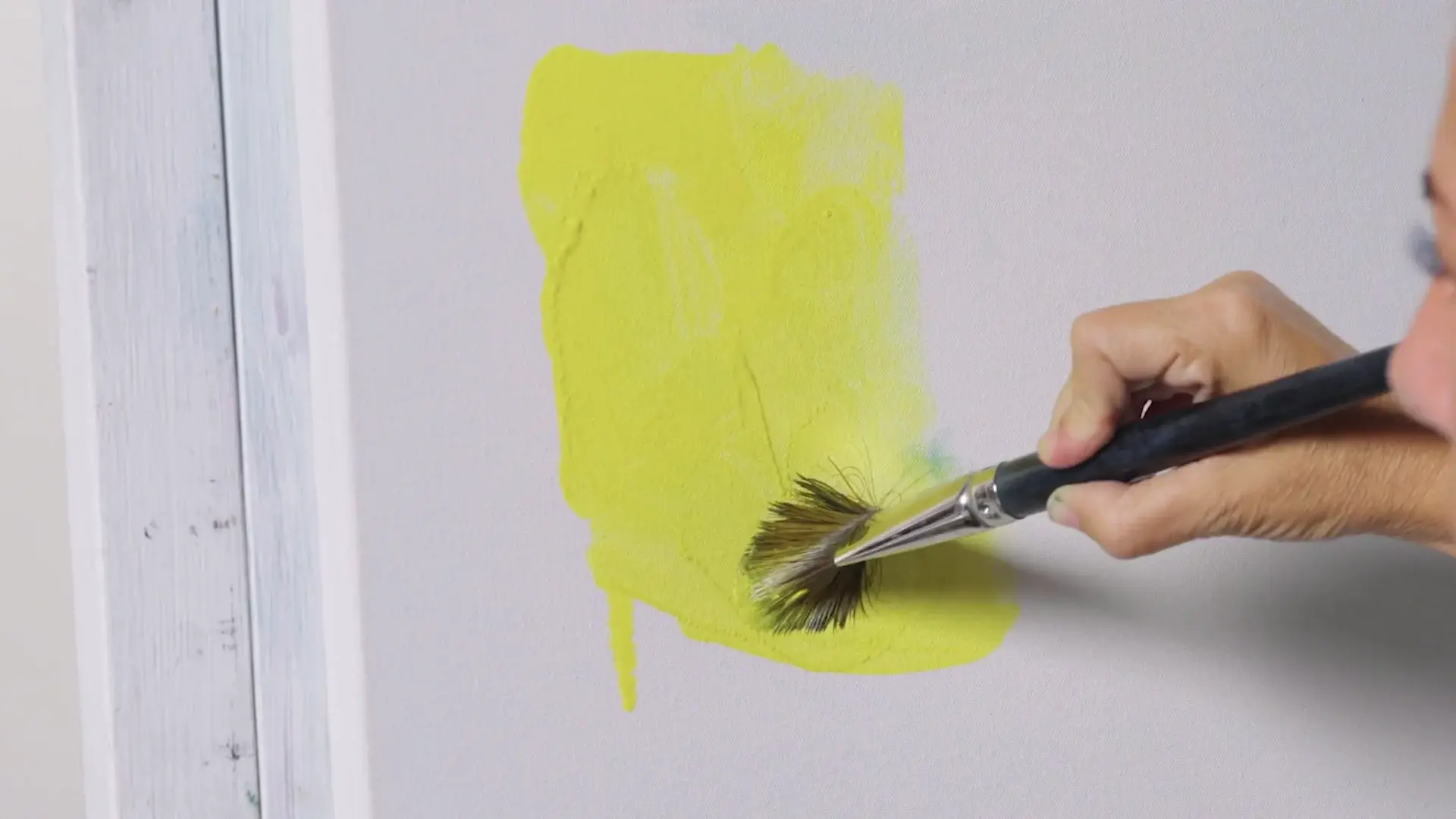 A fan brush scrubbing bright yellow onto the white canvas