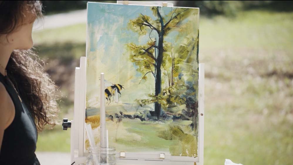 Woman painting on canvas outdoors with bee and tree
