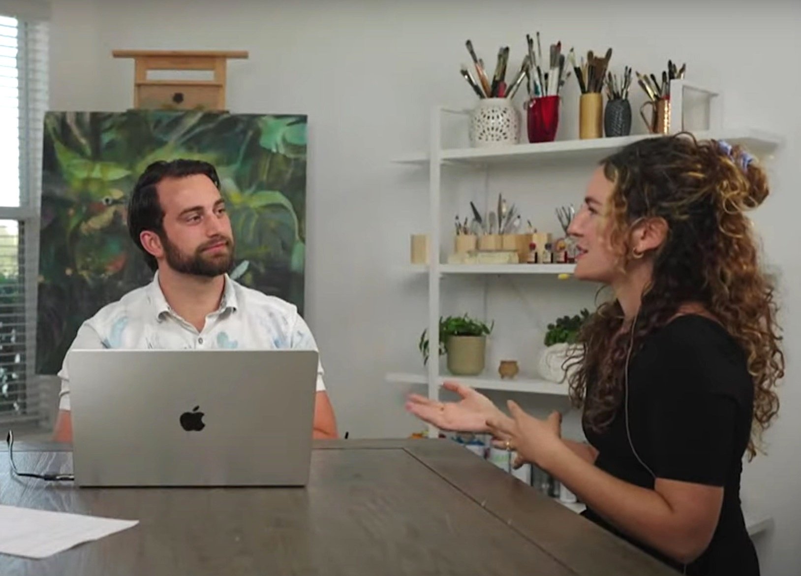 man and women sitting at table with laptop art in background