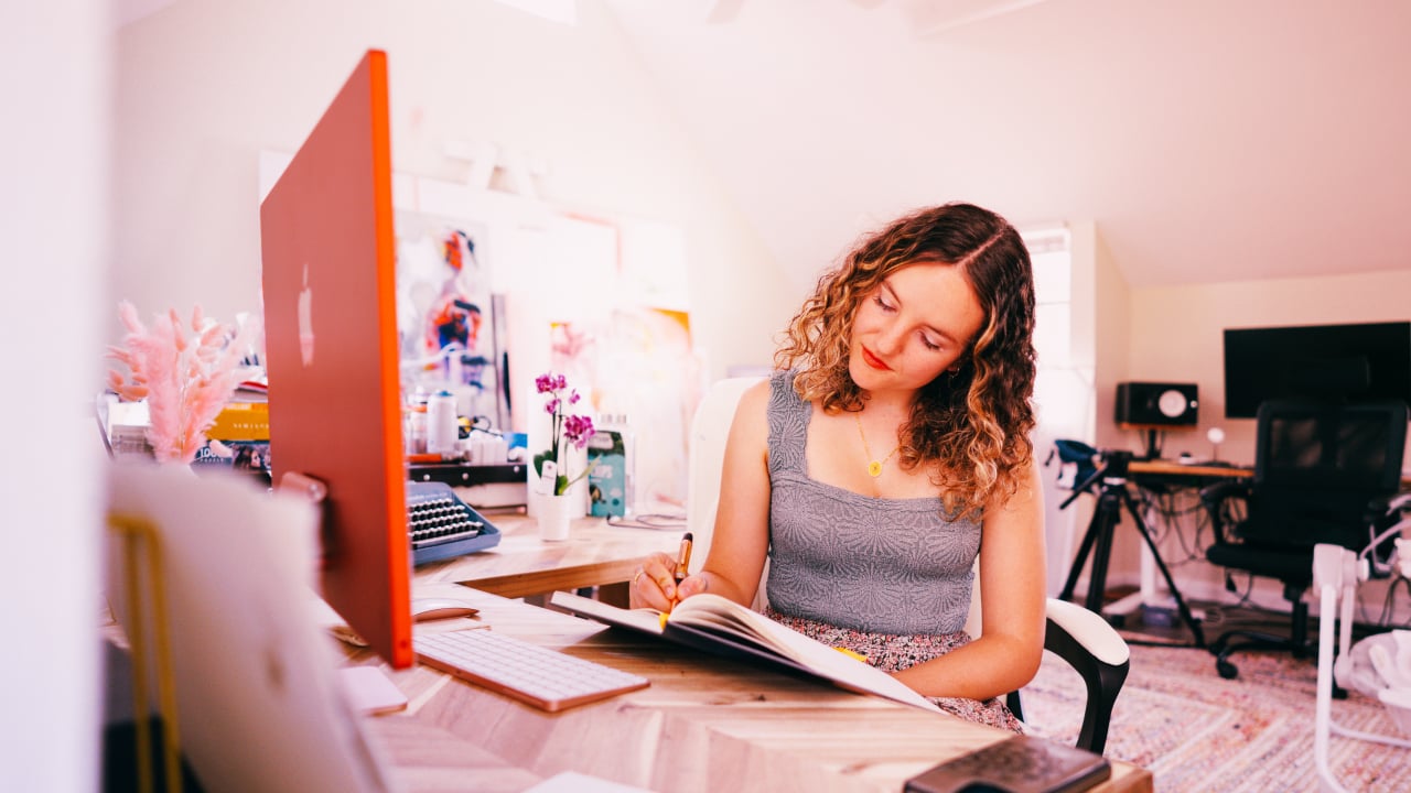 girl sitting in front of orange computer writing on book
