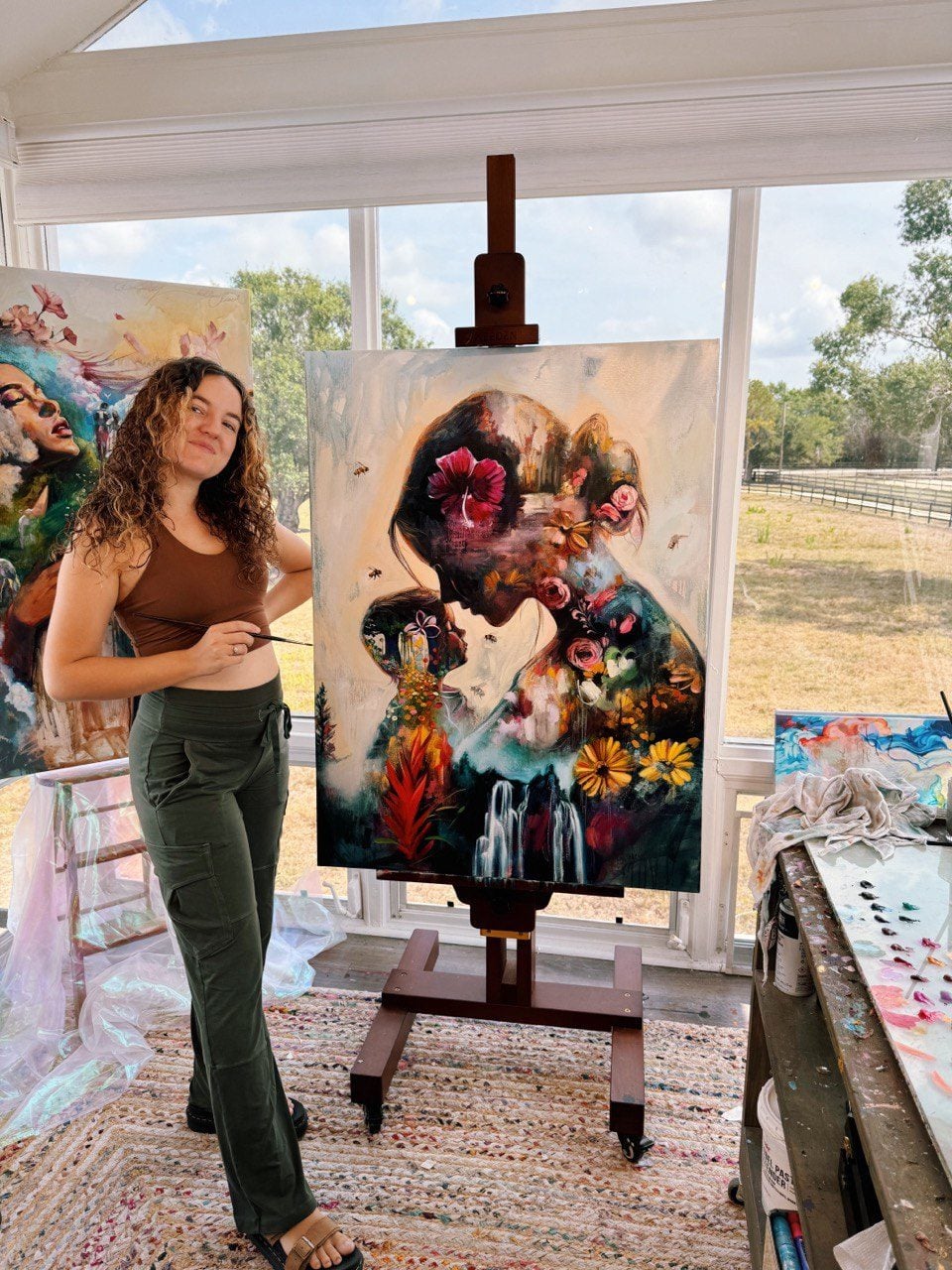 Dimitra Milan standing beside a finished painting on the easel